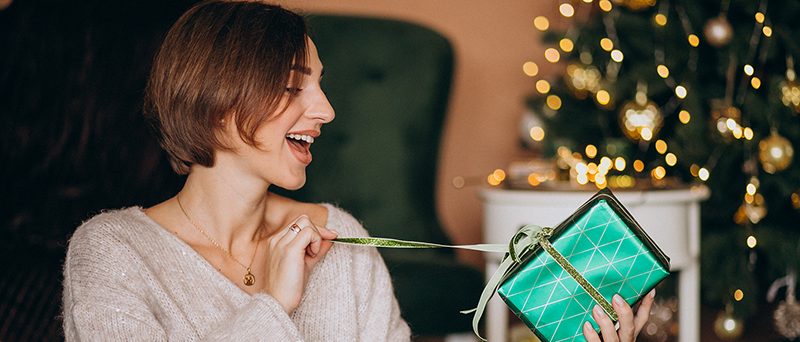 Young woman with Christmas present by the Christmas tree