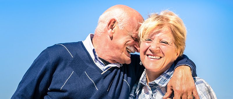 Happy senior couple in love during retirement - Joyful elderly lifestyle with man whispering and smiling with her wife